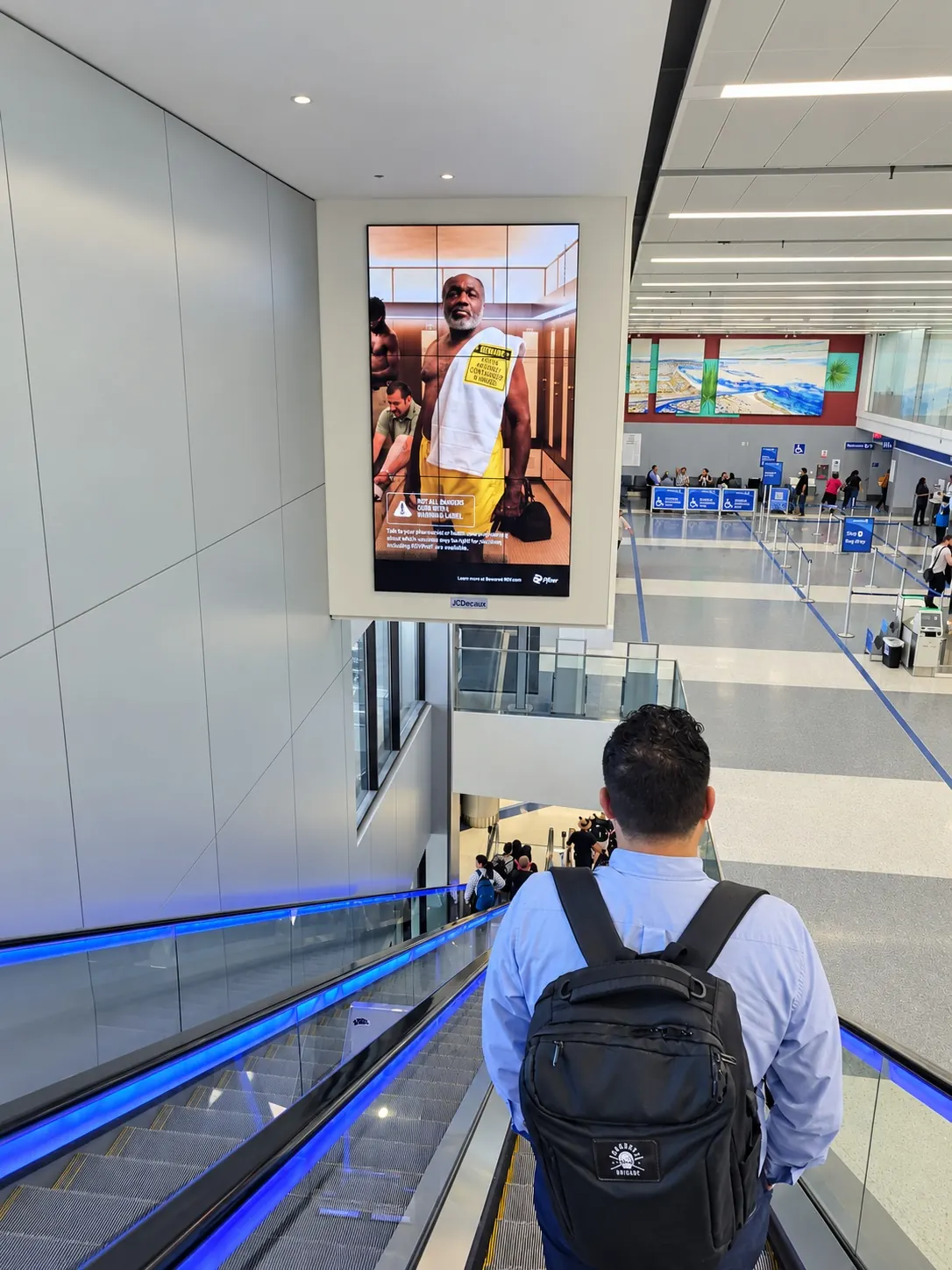 Pfizer digital screen above an arrivals escalator